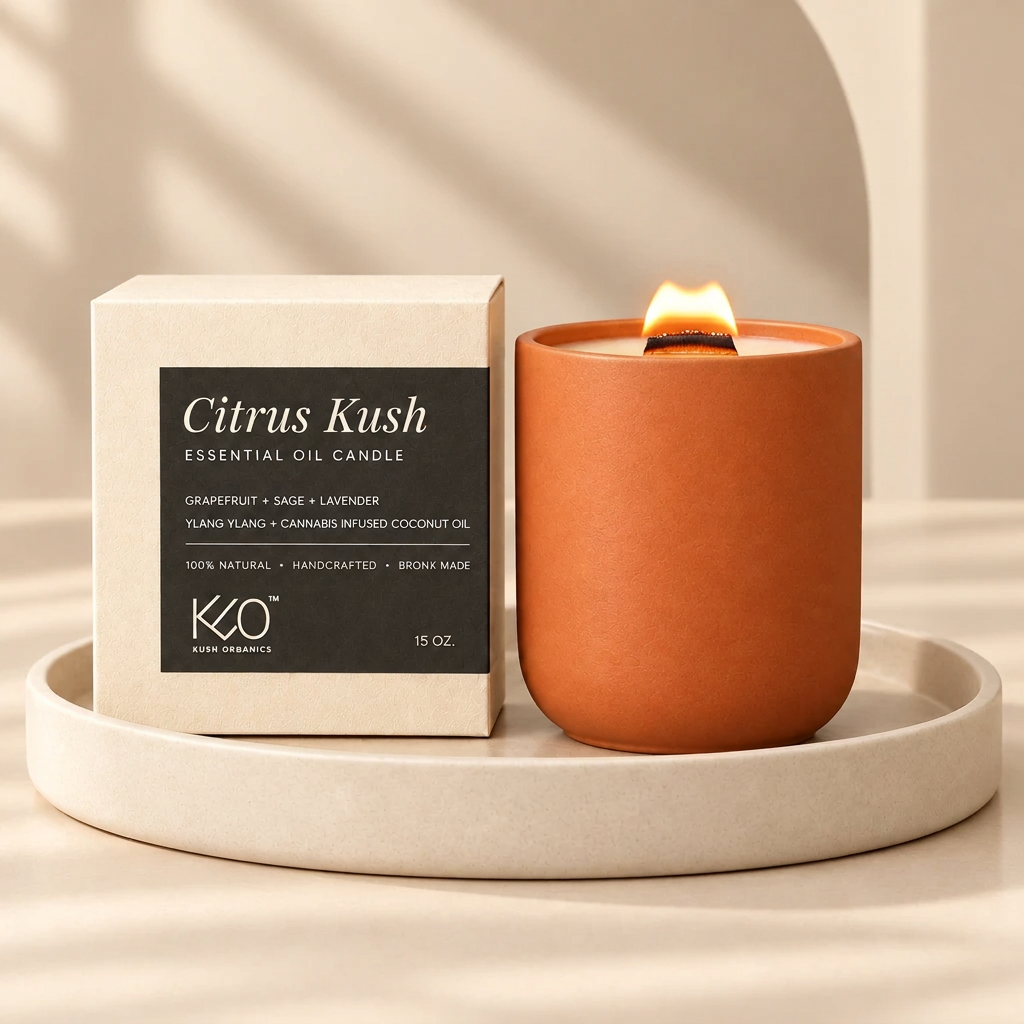 A lit orange terracotta candle in a matte ceramic holder sits beside its cream-colored packaging box with a black label reading 'Citrus Kush' and 'KQO Pure Organics,' placed on a round beige tray against a warm beige background with soft shadows.