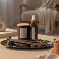 A set of home fragrance products including a candle, a Parfum d'Ambiance spray, and accessories displayed on a metal tray on top of a white surface.
