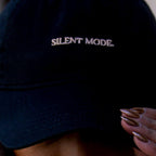 Person wearing a black cap with 'SILENT MODE' text, covering their face.